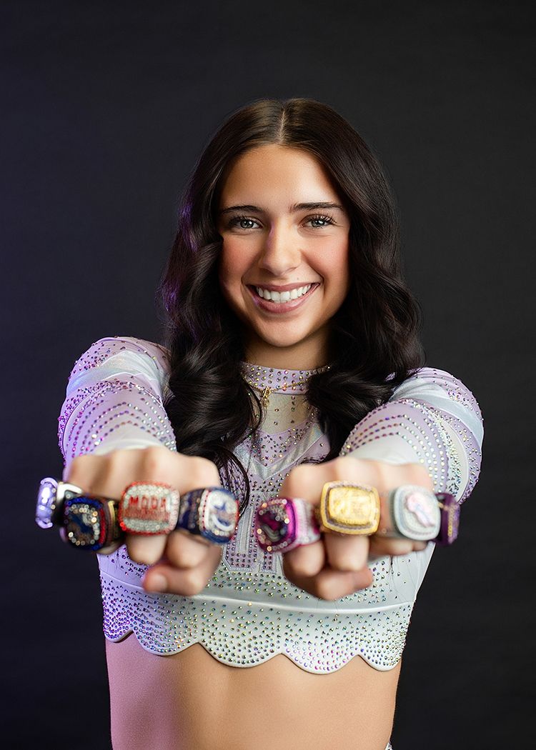 Athlete displays collection of championship rings while wearing sparkly purple and white performance top.