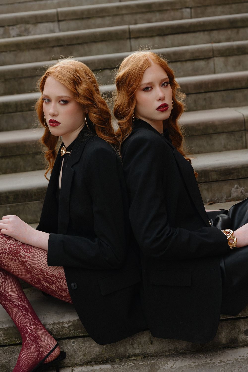 A woman in a black dress with red hair sits gracefully on stone steps in an artistic portrait series.