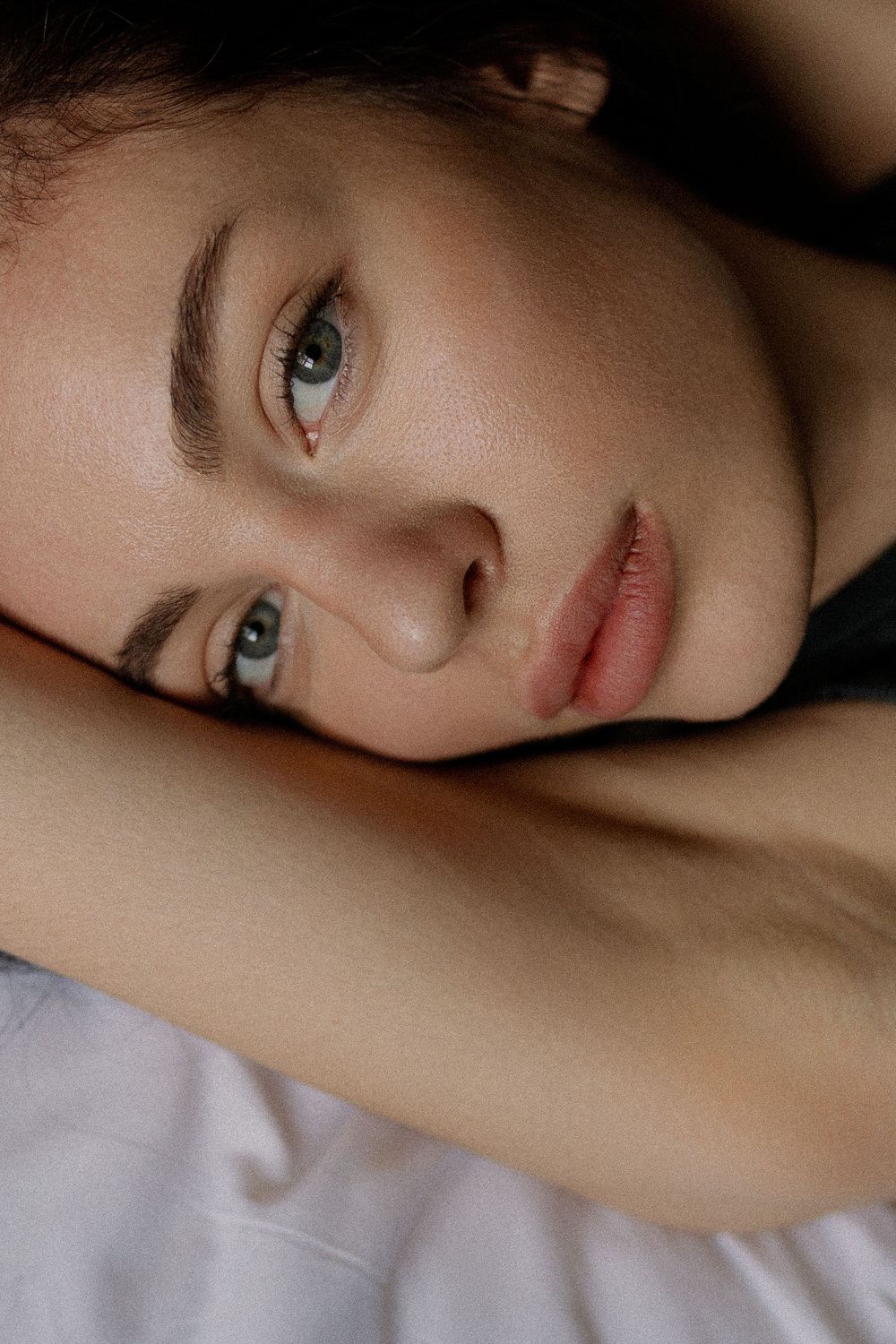 Artistic portrait photo with soft lighting and shadows highlighting delicate features against a light background.