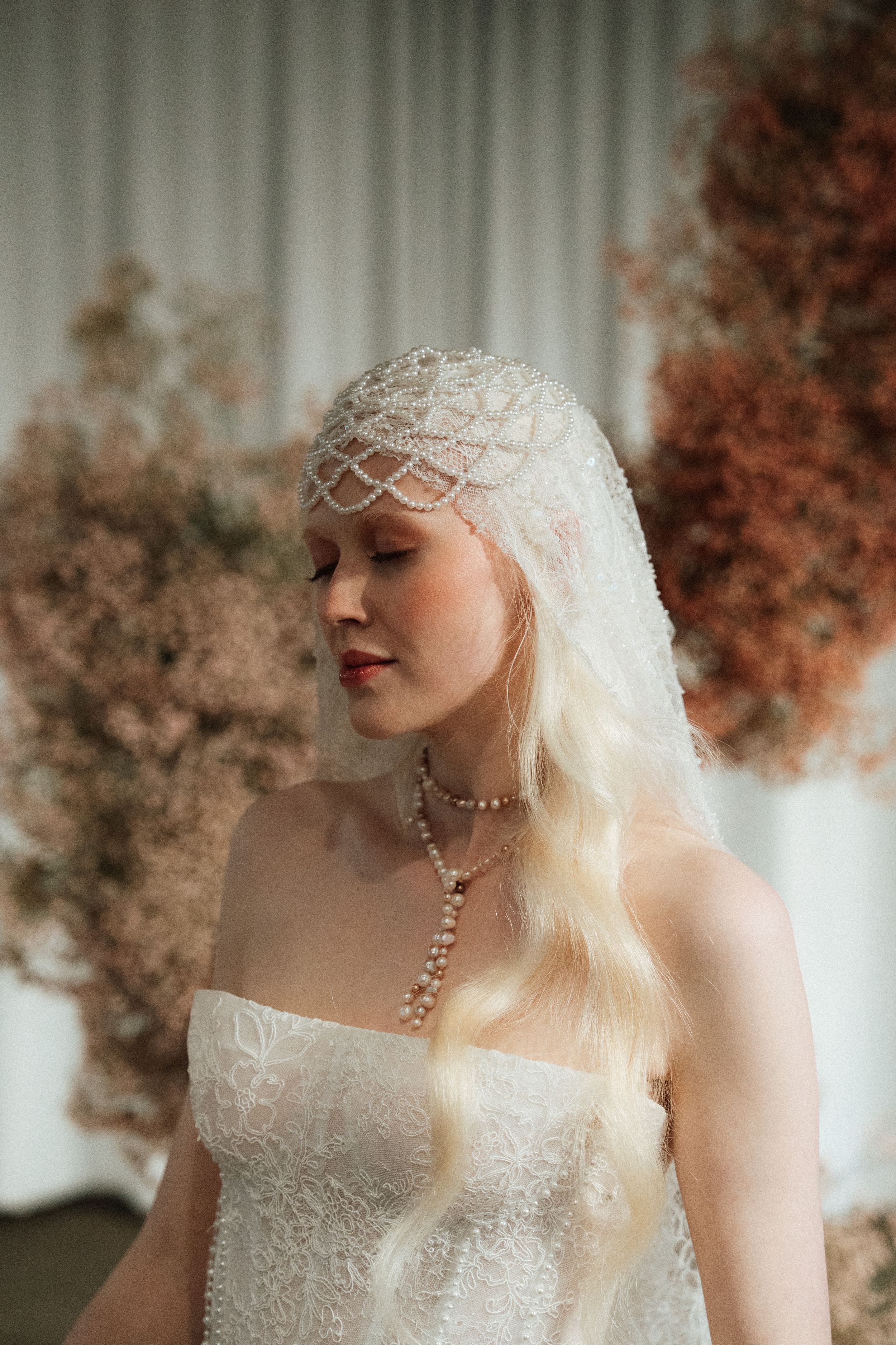 Ethereal bridal portrait featuring delicate lace cap and flowing white gown against autumn-toned background.