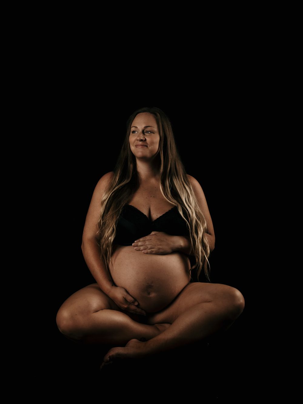 A series of artistic maternity photos showing a pregnant figure in black and white against a dark background.