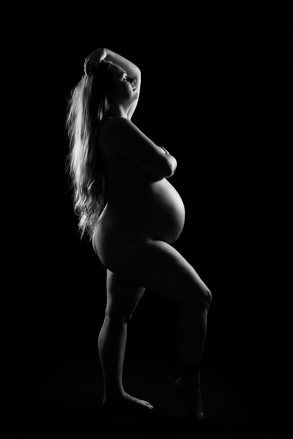 Artistic black and white silhouette series showing a pregnant woman's profile in dramatic lighting.