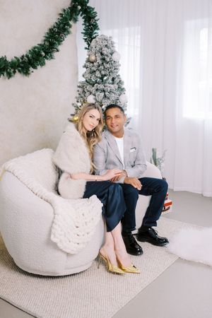 Two people sitting on cozy white bean bag chairs with a decorated Christmas tree in the background.