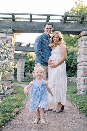 Family in white and blue outfits pose together on stone path during outdoor summer photo session.