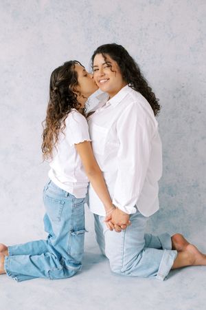Two people in matching white tops and denim jeans sit and interact playfully on a light gray background.