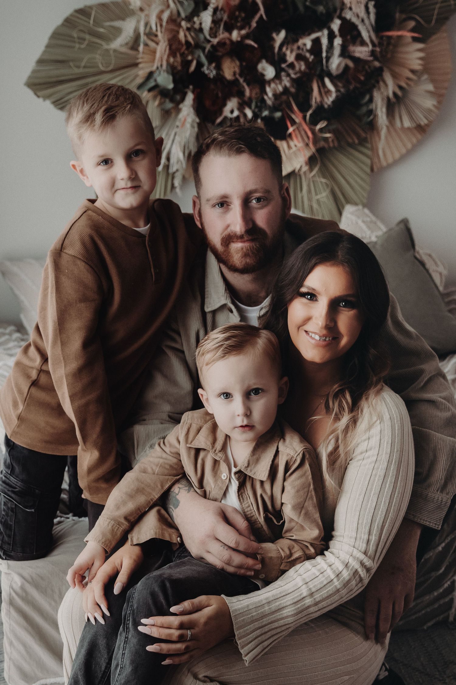 A family wearing neutral tones sits close together for an intimate indoor portrait session with muted lighting.