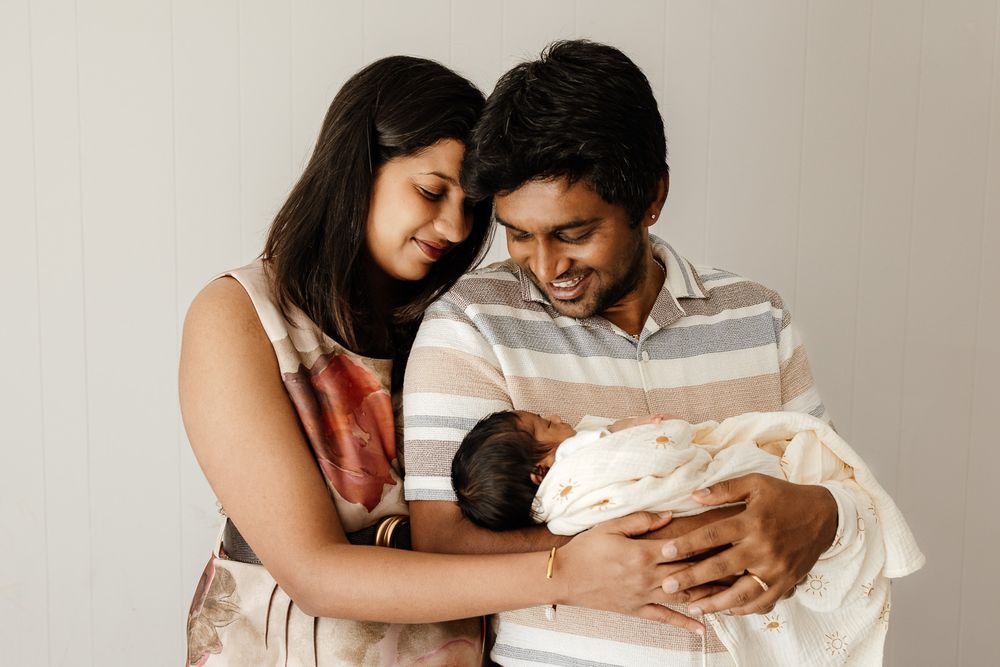 A mother and father smile at their week old newborn baby at their Sunnyvale in-home photoshoot