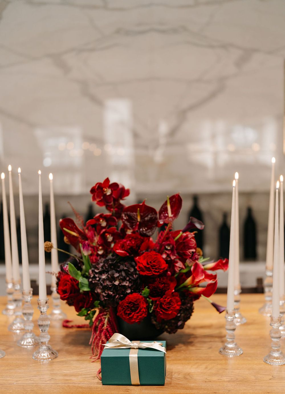 Elegant table setting with white candles and deep red floral arrangements alongside teal gift boxes.