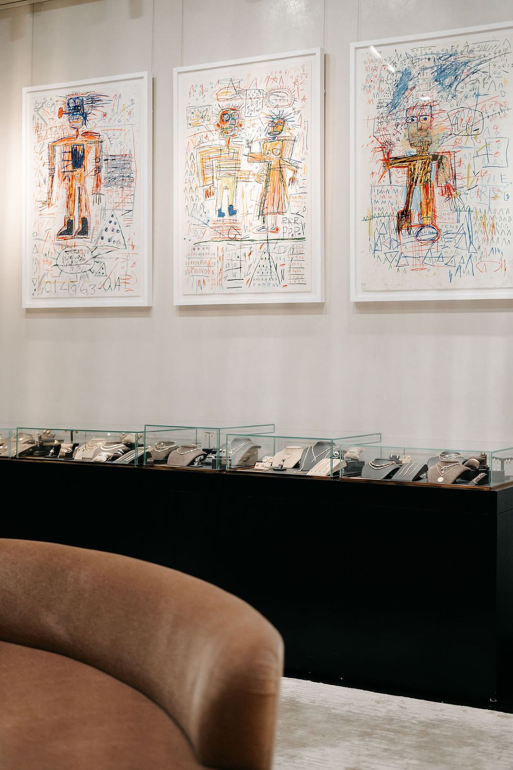 Art gallery wall displaying a series of framed drawings with simple figures in orange and blue on white backgrounds.