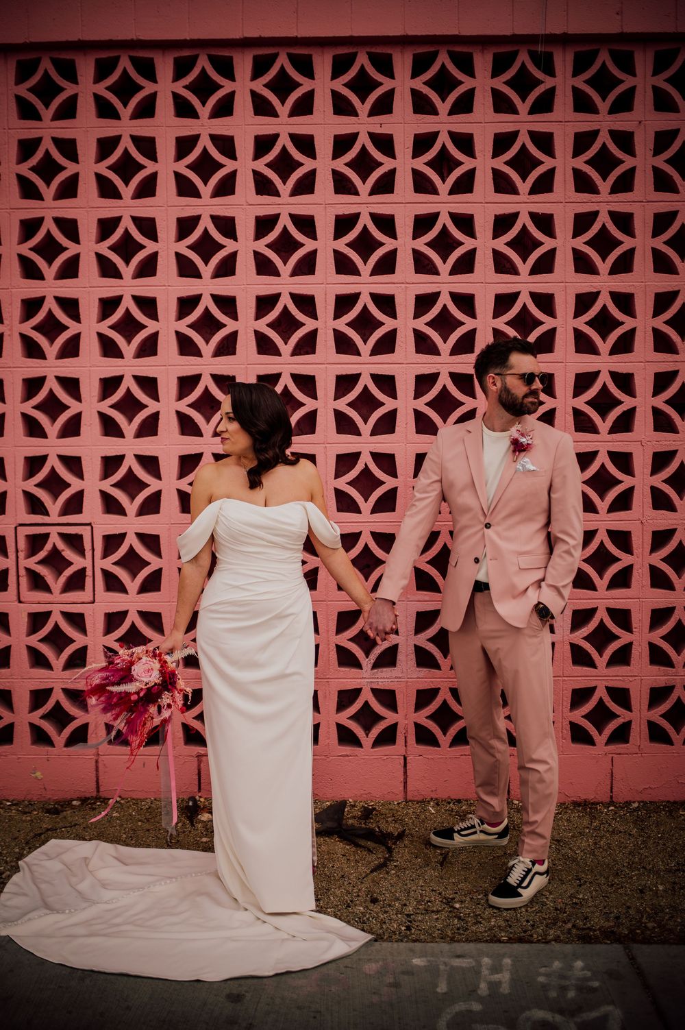 A wedding couple poses in front of a pink decorative breeze block wall in a series of candid moments.