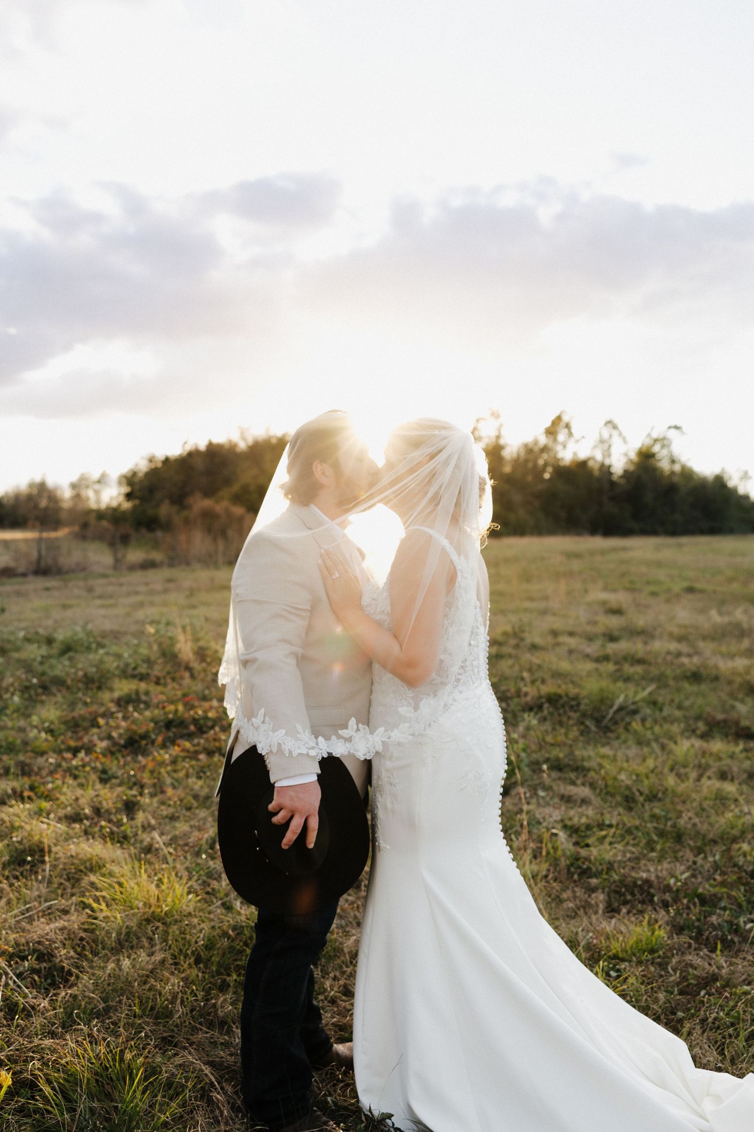 A romantic wedding photo of a couple sharing a kiss near a waterfront with a bridge in the background.