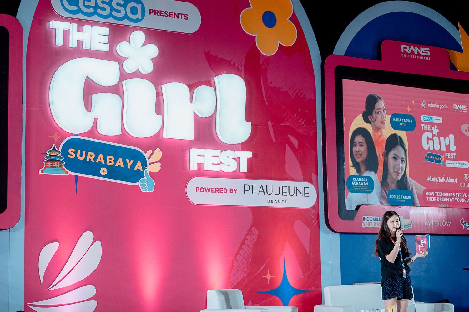 Pink and blue stage backdrop with logos and event branding displayed at an indoor venue.