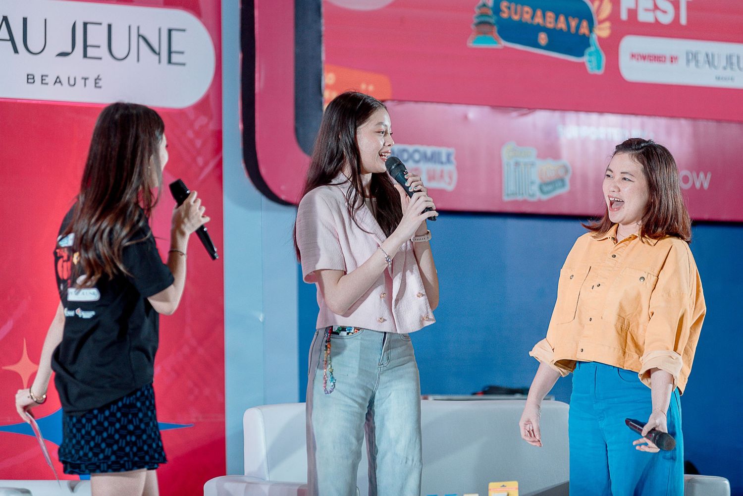 Three women having an animated conversation at a colorful event space with pink and blue walls.
