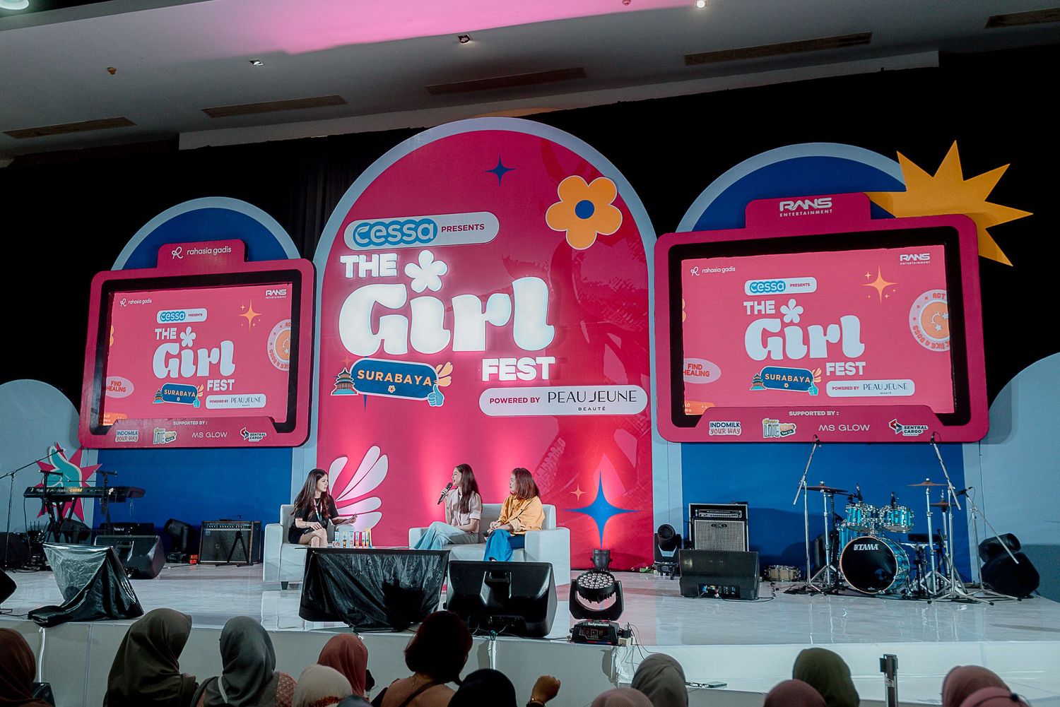 Pink and blue stage setup with three circular display screens and musical instruments at an outdoor performance venue.