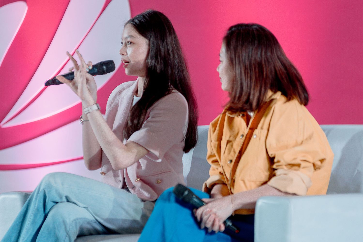People seated at a table engage in conversation against a bright pink background.
