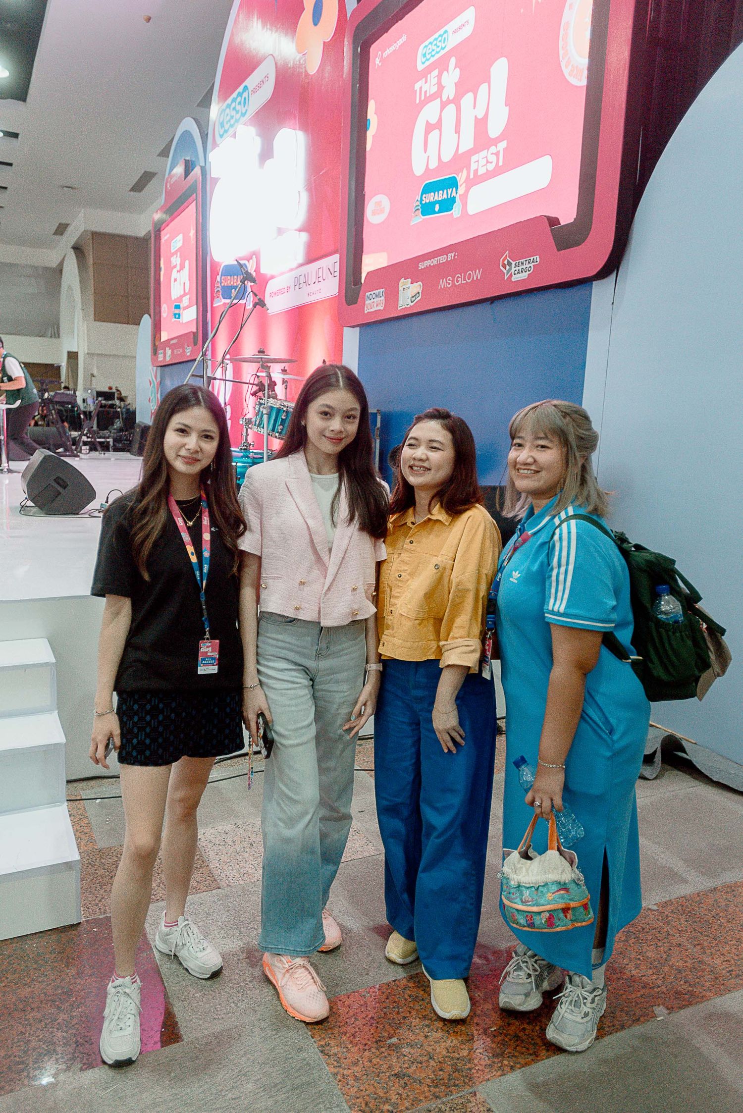 A group of friends pose together against a wall with pink neon signage in what appears to be a mall or shopping center.