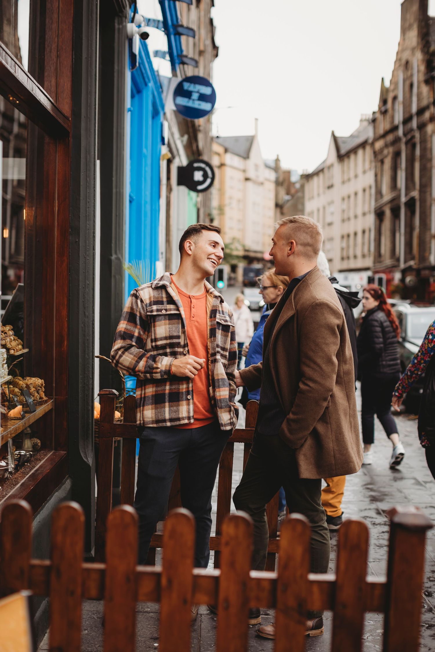 A couple shares intimate moments outside a storefront on a historic city street during an engagement photoshoot.