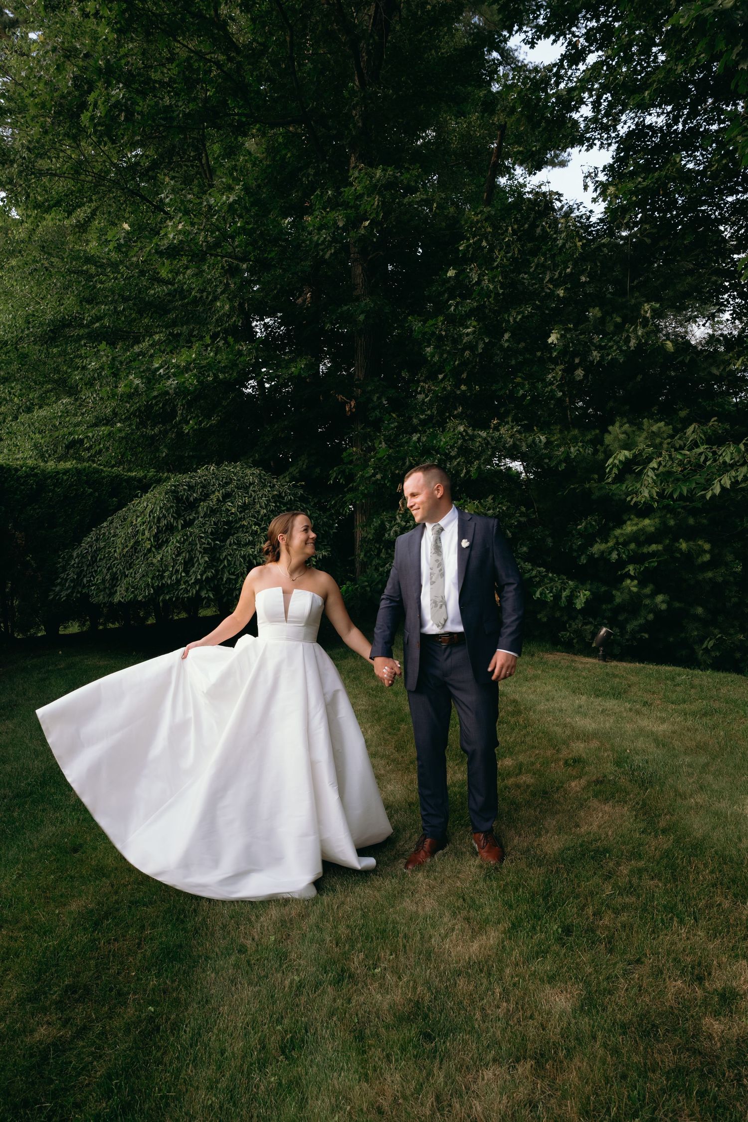 A couple shares a playful moment while feeding each other wedding cake next to a tiered cupcake display at an evening reception.