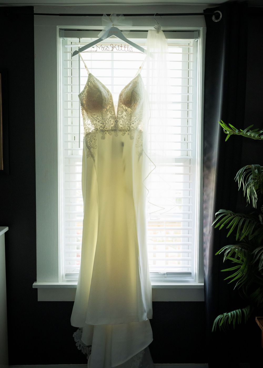 Elegant wedding gown with lace bodice hanging in window light on a hanger.