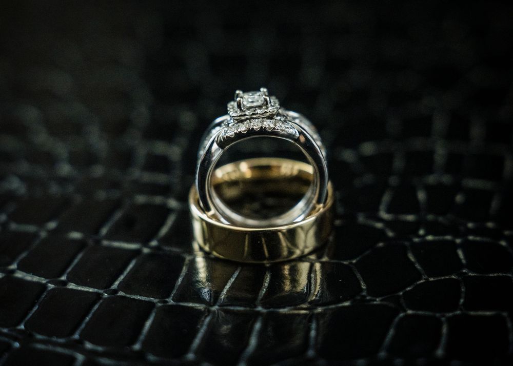 Close-up of sparkling diamond engagement ring and gold wedding band displayed on dark textured surface.