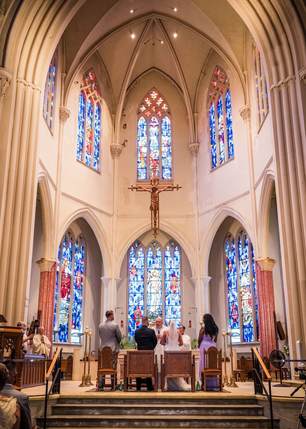 Wedding ceremony at church altar with stunning stained glass windows and crucifix.
