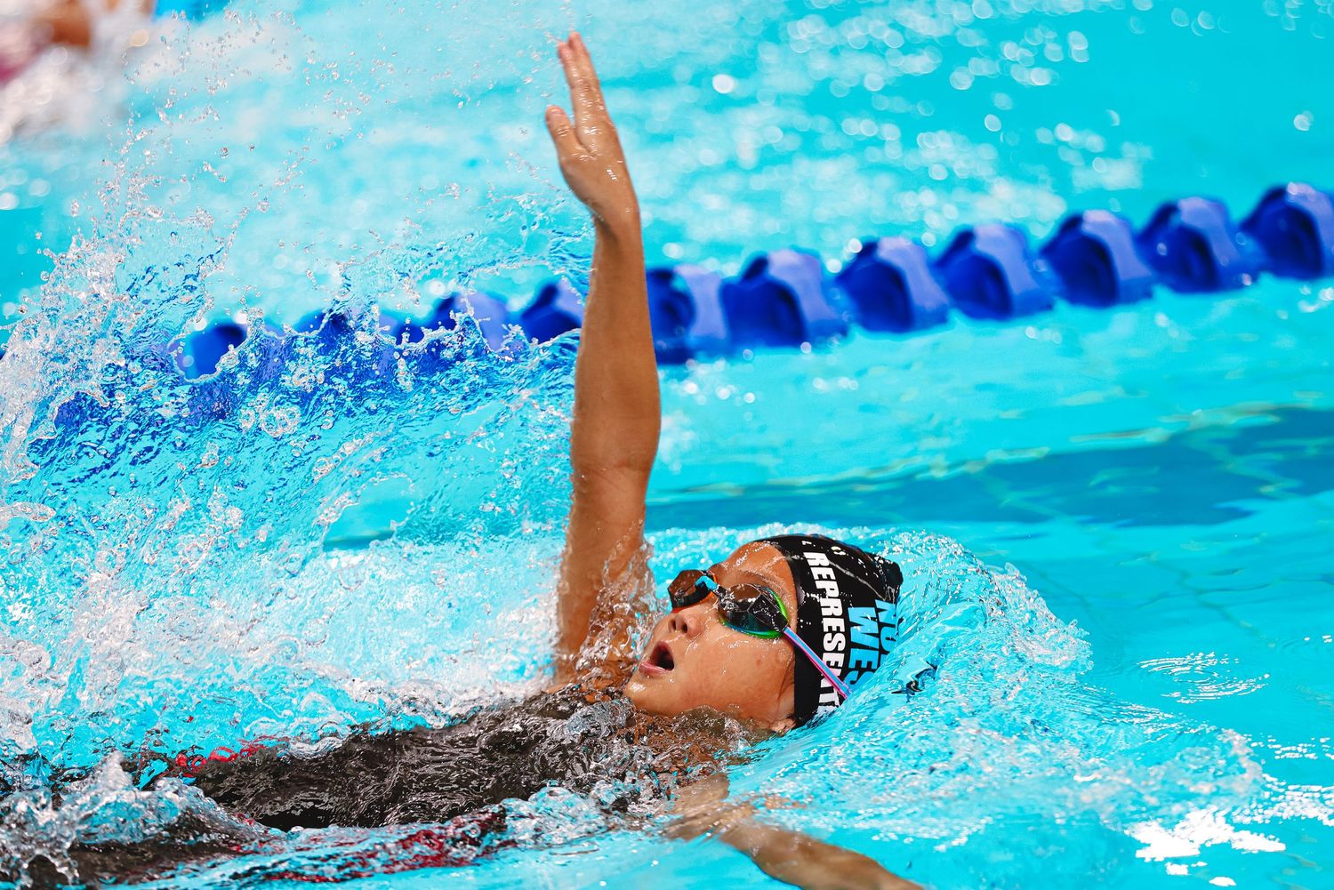 Competitive swimmers dive off starting blocks during a swimming race at an indoor pool.