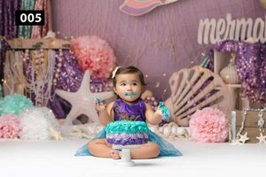 Mermaid themed party setup with seashells, pastel decorations and purple backdrop.