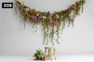 Rustic photography backdrop with hanging floral garland and wooden stool against white wall.