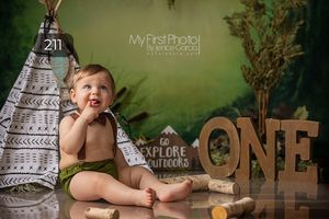 First birthday photoshoot with teepee tent and wooden ONE letters against green backdrop.