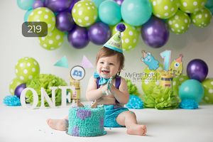 First birthday party setup with teal and purple balloon arch and ONE letters.