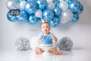 Blue and silver first birthday setup with balloon arch and cake.