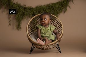 Stylish rattan chair setup with greenery garland backdrop for milestone photography.