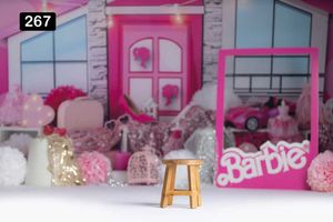 Pink Barbie-themed backdrop with decorative elements and a small wooden stool in the foreground.