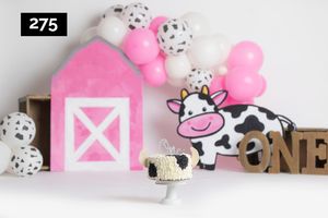 Pink and white party decorations with polka dot balloons and wooden letters arranged against a light background.