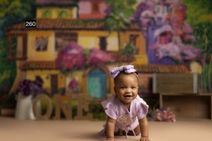 Smiling baby girl in lavender outfit crawling on floor with colorful floral backdrop and ONE sign.