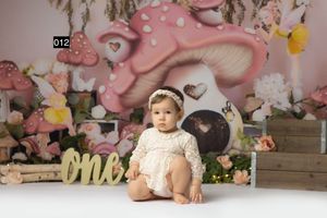Baby girl in lace outfit sits before whimsical mushroom backdrop with flowers and ONE sign for first birthday photo.