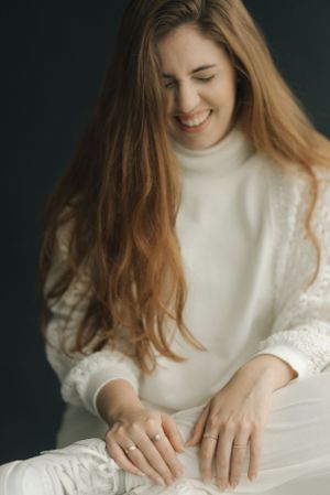 Portrait showing joyful expression wearing a white turtleneck sweater against dark background.