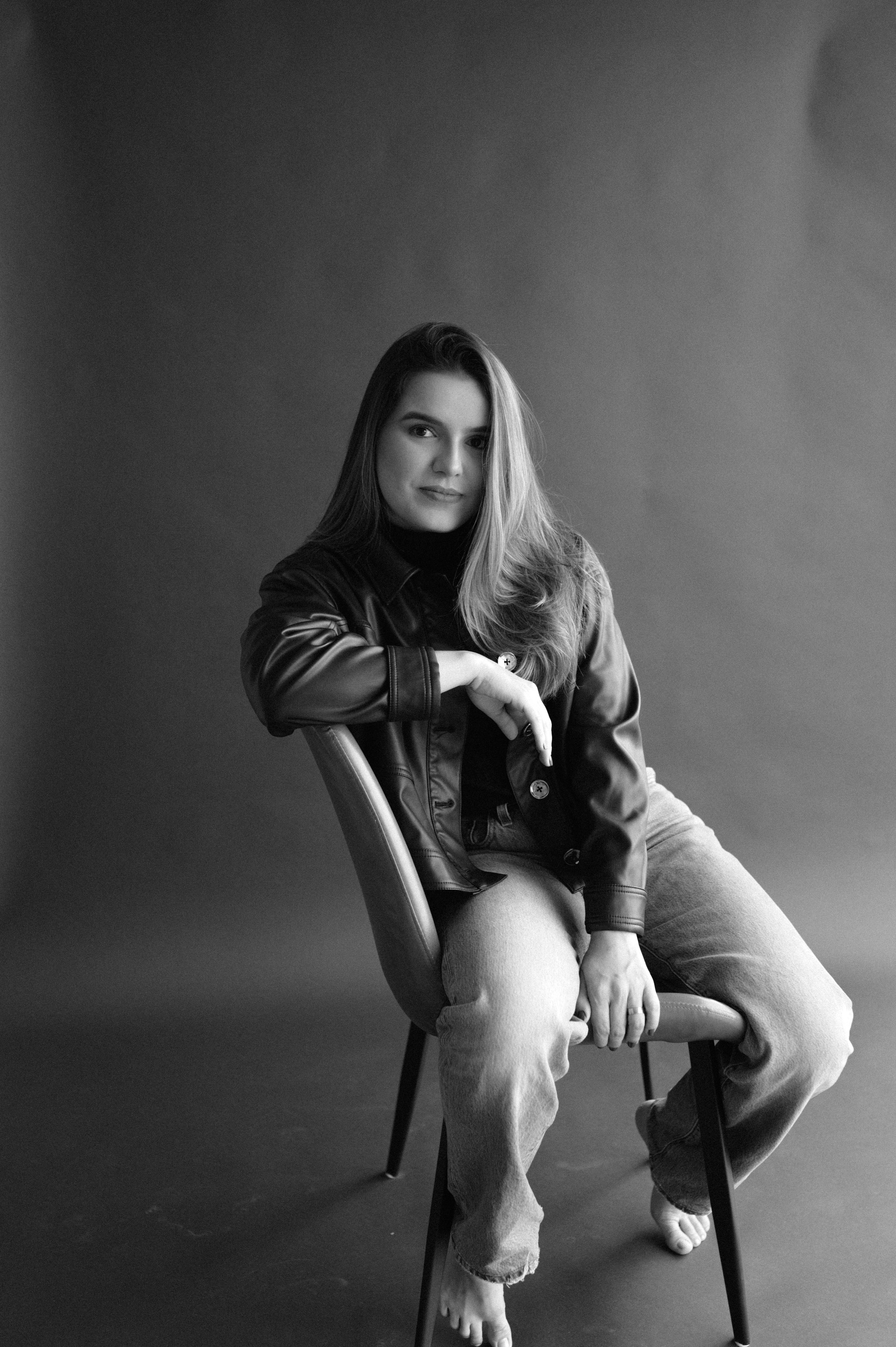Artistic black and white portrait on chair showing casual style and relaxed pose.
