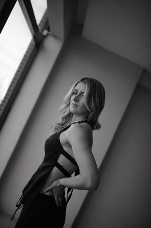 Dramatic black and white photo of a person in an elegant black dress posed near a window.