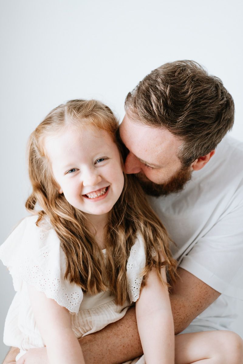 A tender moment captured between parent and child sharing laughter and cuddles against a white background.