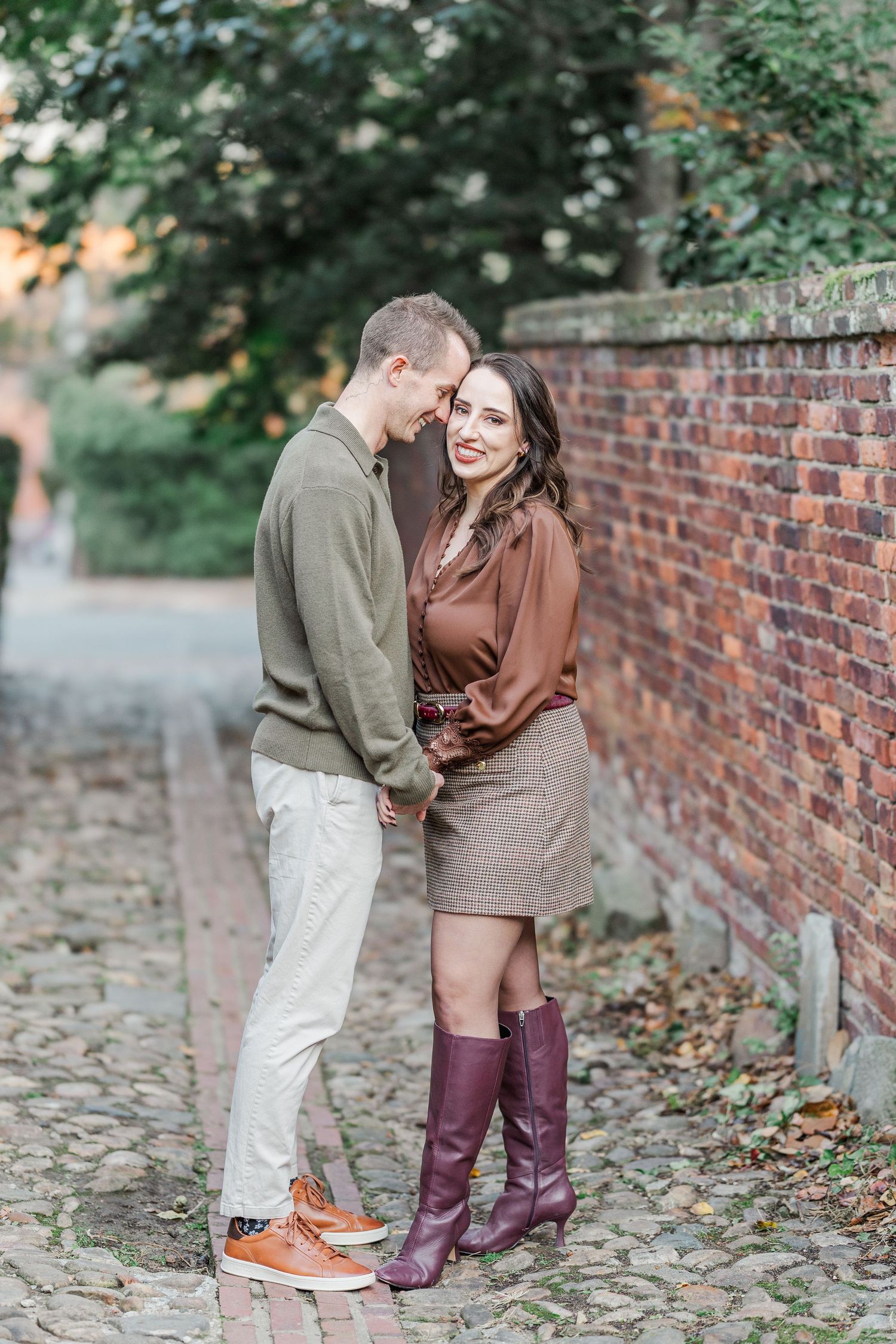 A couple shares a romantic moment on a cobblestone path next to a brick wall during an autumn engagement photoshoot.