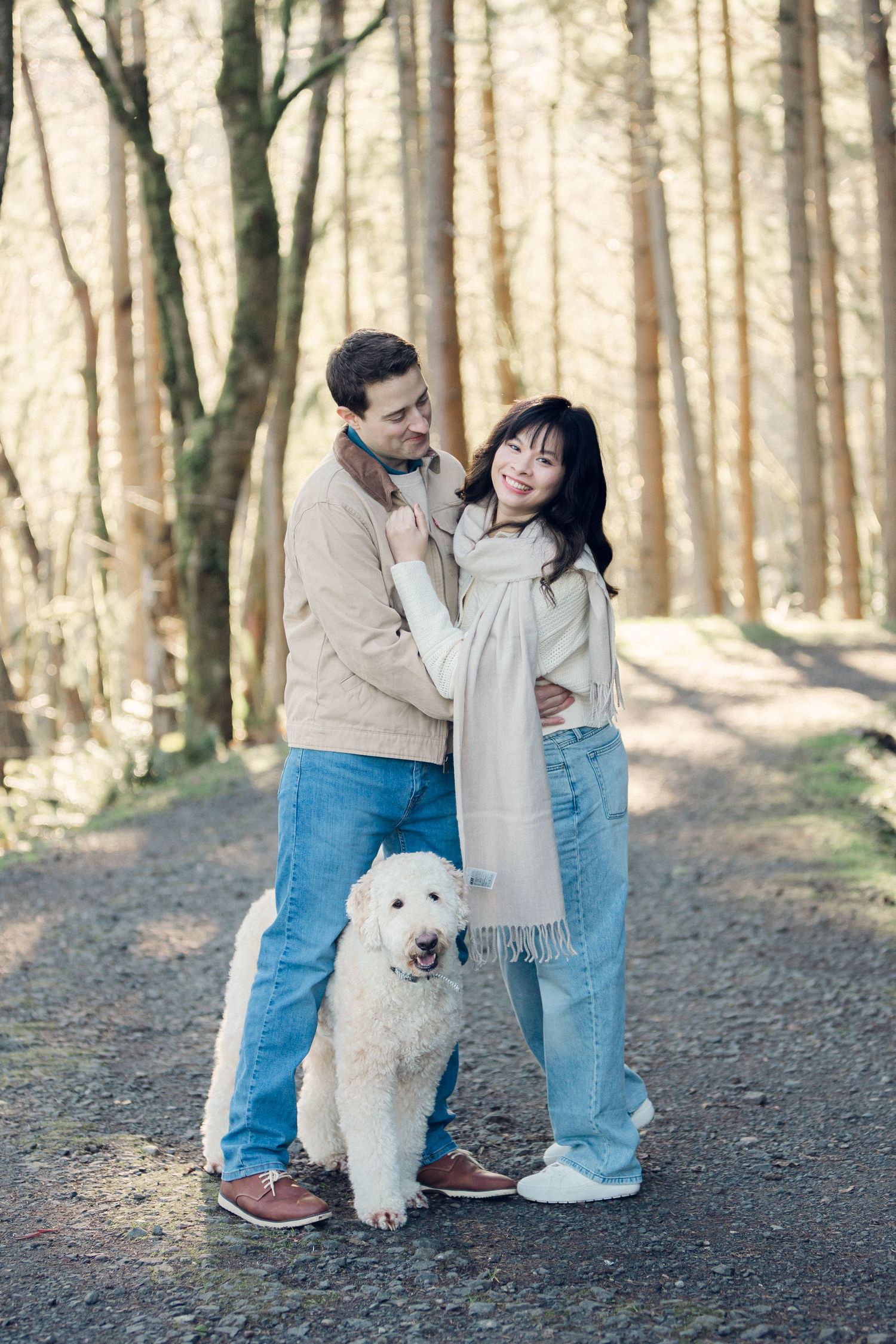 A couple and their fluffy white dog share tender moments together while walking on a forest trail in autumn.