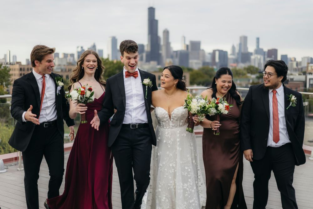 Wedding party stands together on rooftop with Chicago skyline visible in background.