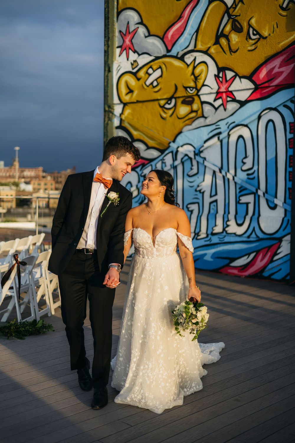 A couple in wedding attire poses together on a deck with colorful Chicago street art mural in the background.