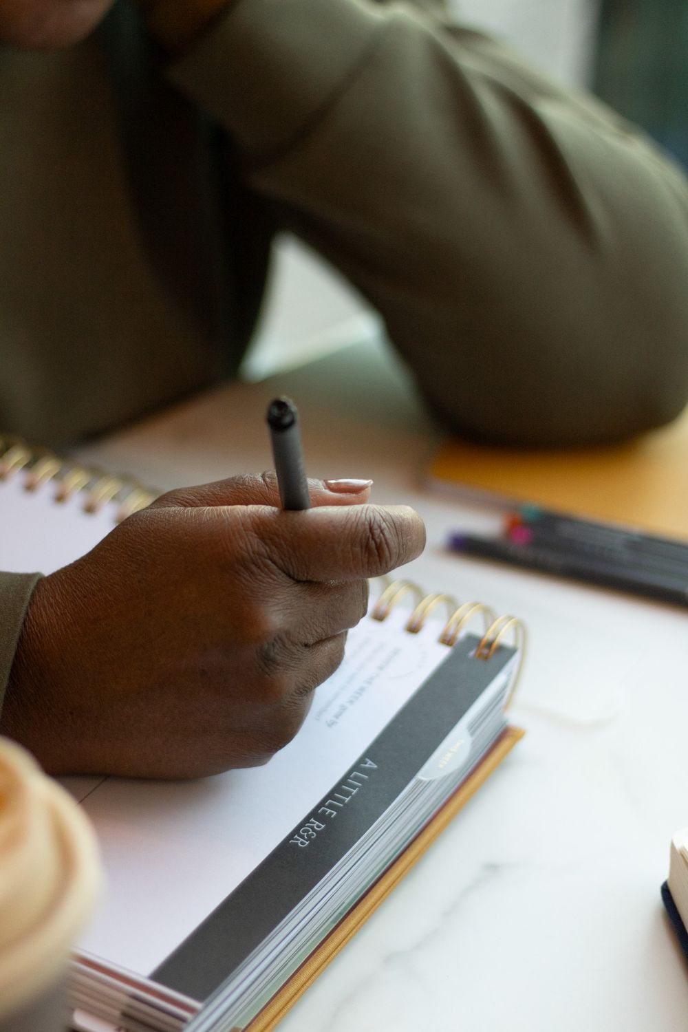 Close-up of hand holding pen while writing in spiral notebook.