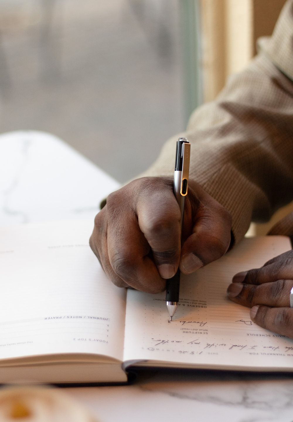 Close-up of hands writing in notebook with pen on white surface.