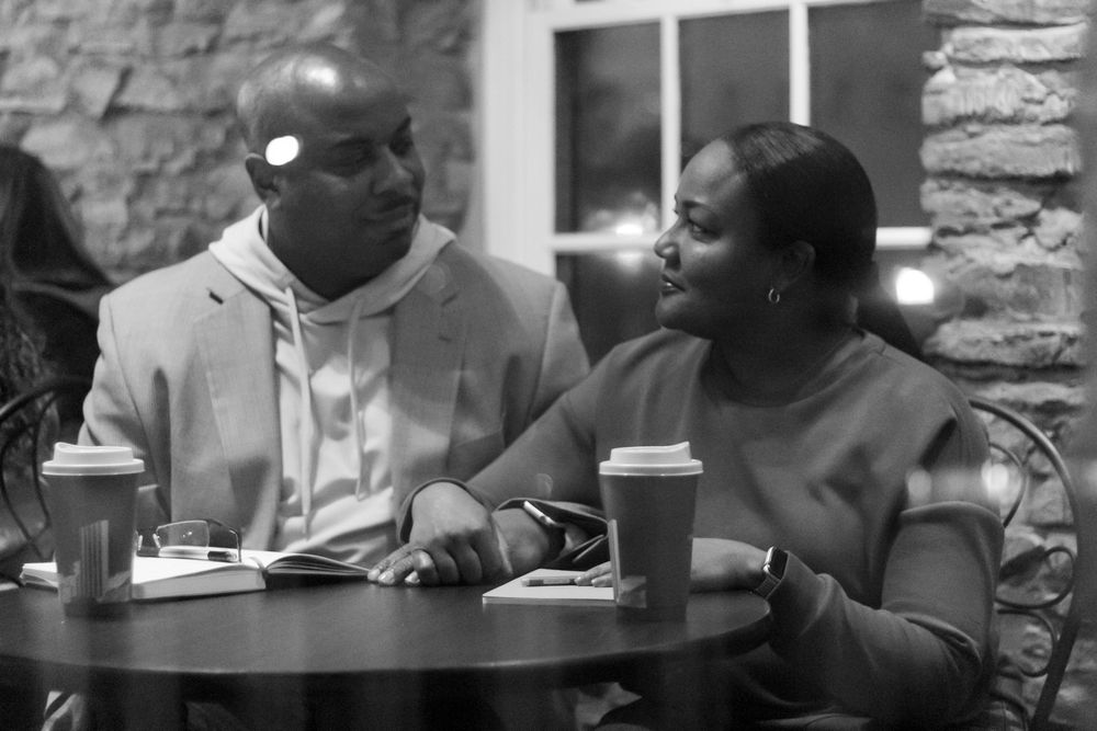 People sharing conversation at a cafe table with stone wall background.