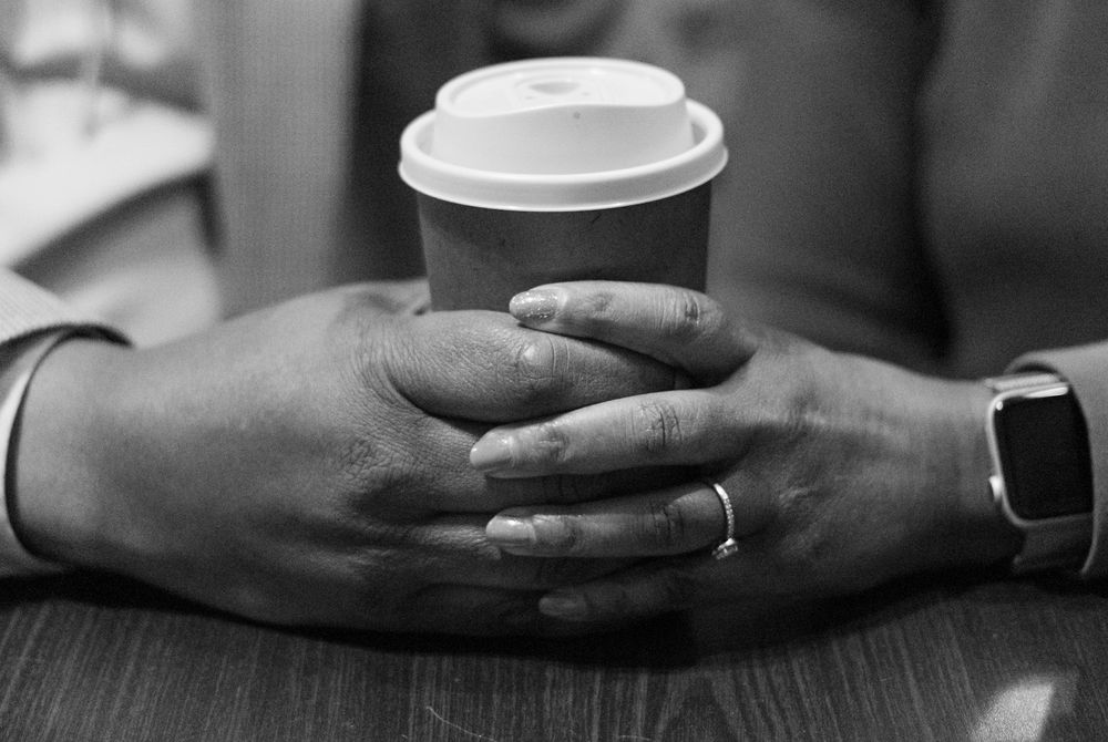 Close-up of hands holding disposable coffee cups on a dark surface.