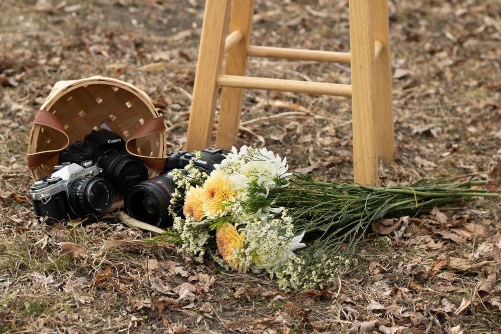 Camera and floral bouquet arranged with wicker basket on ground.
