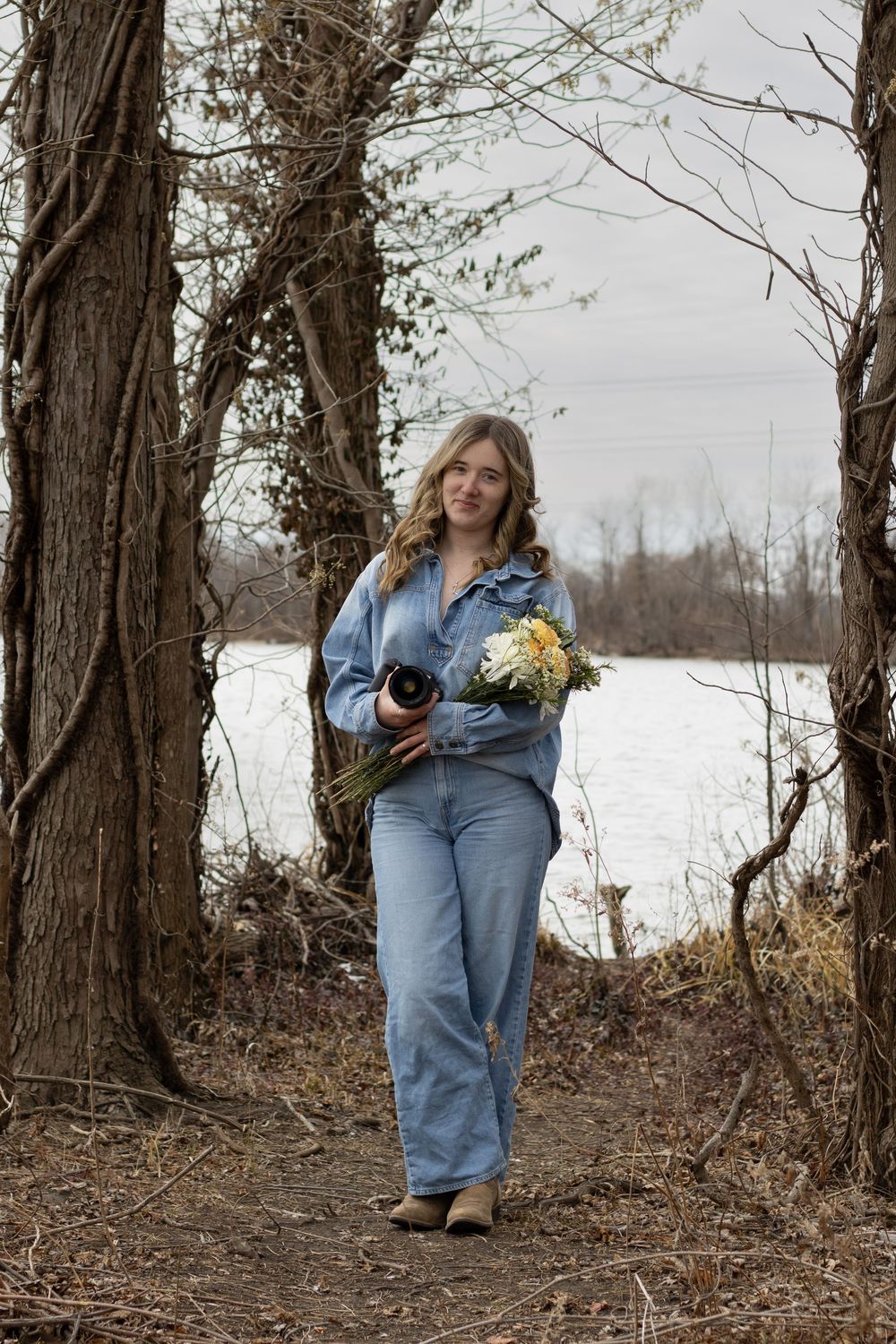 Photographer carrying camera and yellow flowers walks through snowy winter landscape.